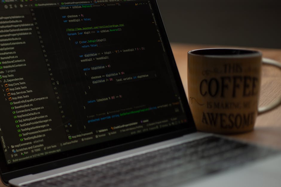 A person using a laptop with a dark-themed code editor open on the screen, displaying lines of programming code in green, blue, and white text. The individual is typing with both hands, with the right